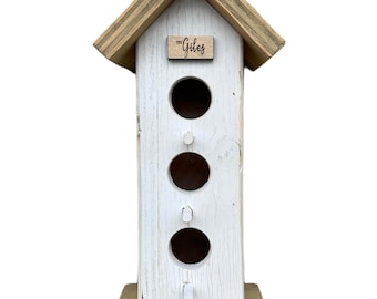 May include: White wooden birdhouse with a brown roof and a sign that says "The Giles". The birdhouse has three nesting holes.