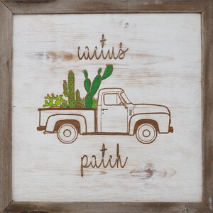 May include: A white wooden sign with a brown frame features a line drawing of a pickup truck carrying a variety of cacti. The text "cactus patch" is written below the truck and the text "cactus" is written above the truck.