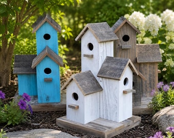Könnte beinhalten: Eine Ansammlung von hölzernen Vogelhäusern in mehrstöckigem Design mit verwitterten grauen Dächern. Die Strukturen sind in leuchtendem Blau, Weiß und Naturholztönen gehalten und verfügen jeweils über ein rundes Einflugloch und eine Sitzstange.