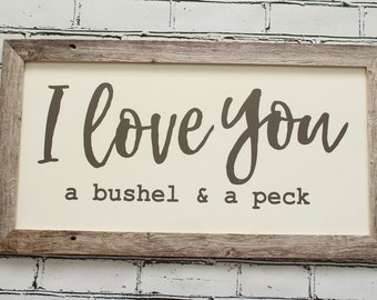 May include: A rustic wooden framed sign with the text "I love you a bushel & a peck" in brown lettering on a cream background.