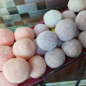 May include: A close-up of a tray of round, sugared candies in pink, purple, and white. The candies are arranged in a circular pattern and are covered in a fine layer of sugar.