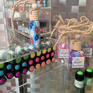 May include: Assortment of colorful glass bottles with floral patterned lids, some in clear boxes with the text "Scent Scatterers".  The bottles are arranged on a clear acrylic shelf with colorful dots.