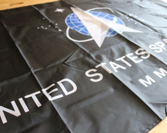 May include: A black flag with the words "UNITED STATES SPACE FORCE MMXIX" in white text. The flag also features a white rocket ship with a blue globe in the background.
