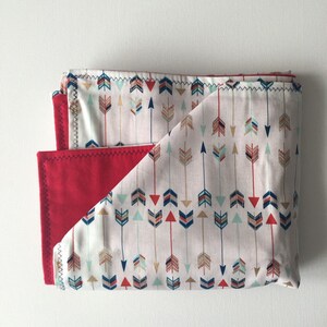 May include: A folded red and white baby blanket with a pattern of colorful arrows on one side.