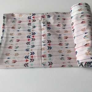 May include: A pink baby blanket with a pattern of colorful arrows. The blanket is rolled up and ready to be used.