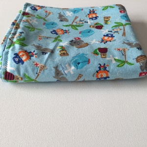 Pode incluir: Um cobertor de beb&ecirc; azul claro com uma estampa de tema pirata. A estampa apresenta piratas, papagaios, ba&uacute;s do tesouro e palmeiras.