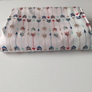 May include: A folded fabric with a white background and a repeating pattern of colorful arrows. The arrows are in shades of red, blue, green, and gold.