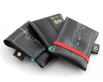 May include: Three black leather wallets made from recycled bicycle inner tubes. The wallets have different brands printed on them, including "Schwalbe" and "Hutchinson".