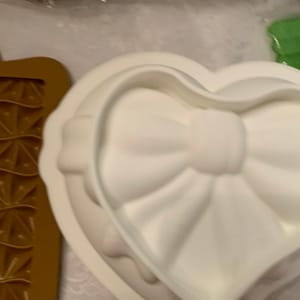 May include: White silicone mold shaped like a heart with a bow in the center. The mold is designed for baking or making crafts.