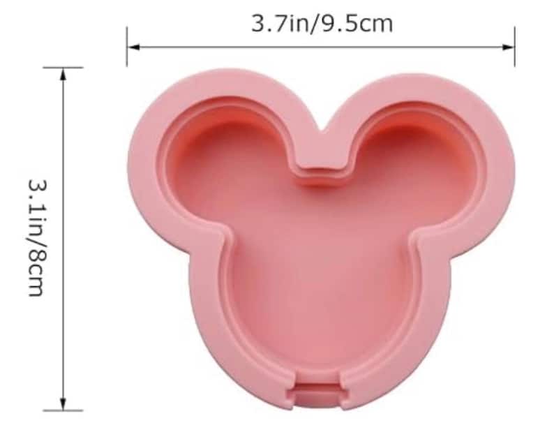 May include: A light pink silicone mould shaped like a mouse head with rounded ears. The mould features a recessed centre and raised edges. Dimension lines indicate a width of 9.5 cm and a height of 8 cm for the overall structure.