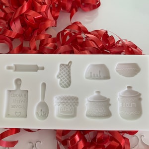 May include: White silicone baking mould with eight different shapes, including a rolling pin, oven mitt, bowl, and a sign that reads "Baked with Love".