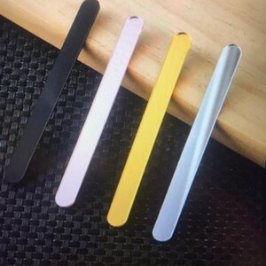 May include: Four thin metal rods in different colours: black, pink, gold, and light blue. The rods are arranged in a diagonal pattern on a wooden surface.