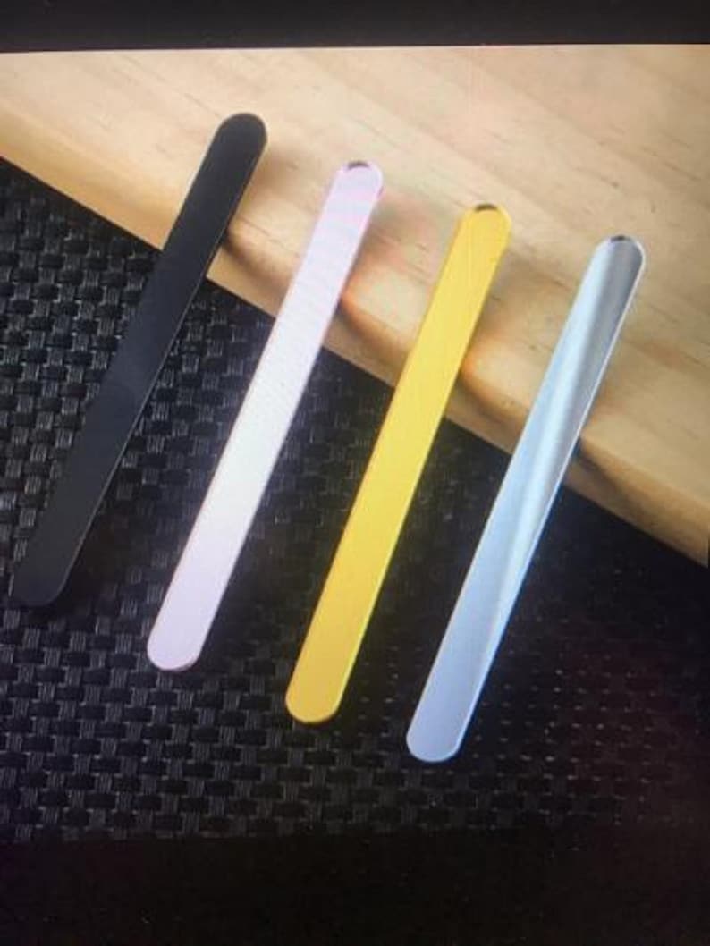 May include: Four thin metal rods in different colours: black, pink, gold, and light blue. The rods are arranged in a diagonal pattern on a wooden surface.