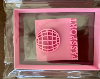 Peut inclure: Un cadre en plastique rose avec un insert en plastique rose. L'insert présente un motif de globe terrestre et le mot "PASSPORT" imprimé sur le côté droit.