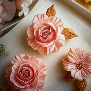 Peut inclure: Gros plan sur trois d&eacute;corations florales roses claires d&eacute;taill&eacute;es avec des centres roses plus fonc&eacute;s et des feuilles marron. Les fleurs sont dispos&eacute;es sur une surface de couleur claire, avec une esth&eacute;tique douce et artistique. Les fleurs sont probablement faites d'un mat&eacute;riau d&eacute;licat.