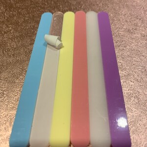May include: Six nail files in different colours: light blue, white, yellow, pink, white, and purple. The files are arranged in a row from left to right.