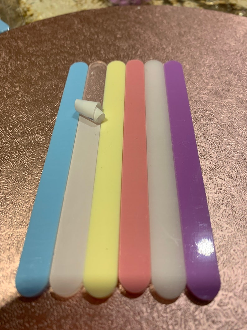 May include: Six nail files in different colours: light blue, white, yellow, pink, white, and purple. The files are arranged in a row from left to right.