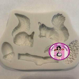 May include: A white silicone mold featuring two squirrels, an acorn, a pine cone, and a branch. The mold is designed for creating detailed edible decorations. The image includes a logo for Nene's Sweet Supplies.