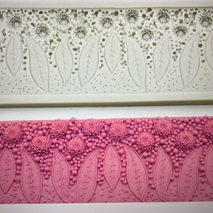 May include: A white silicone mold with a design of leaves and flowers. The mold is shown with pink fondant pressed into it, showing the design in detail.