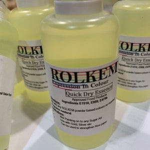May include: A clear plastic bottle containing a yellow liquid. The bottle is labelled "ROLKEM Expression In Colour Quick Dry Essence Approved Food Products Ingredients E1510, E959, E479b".