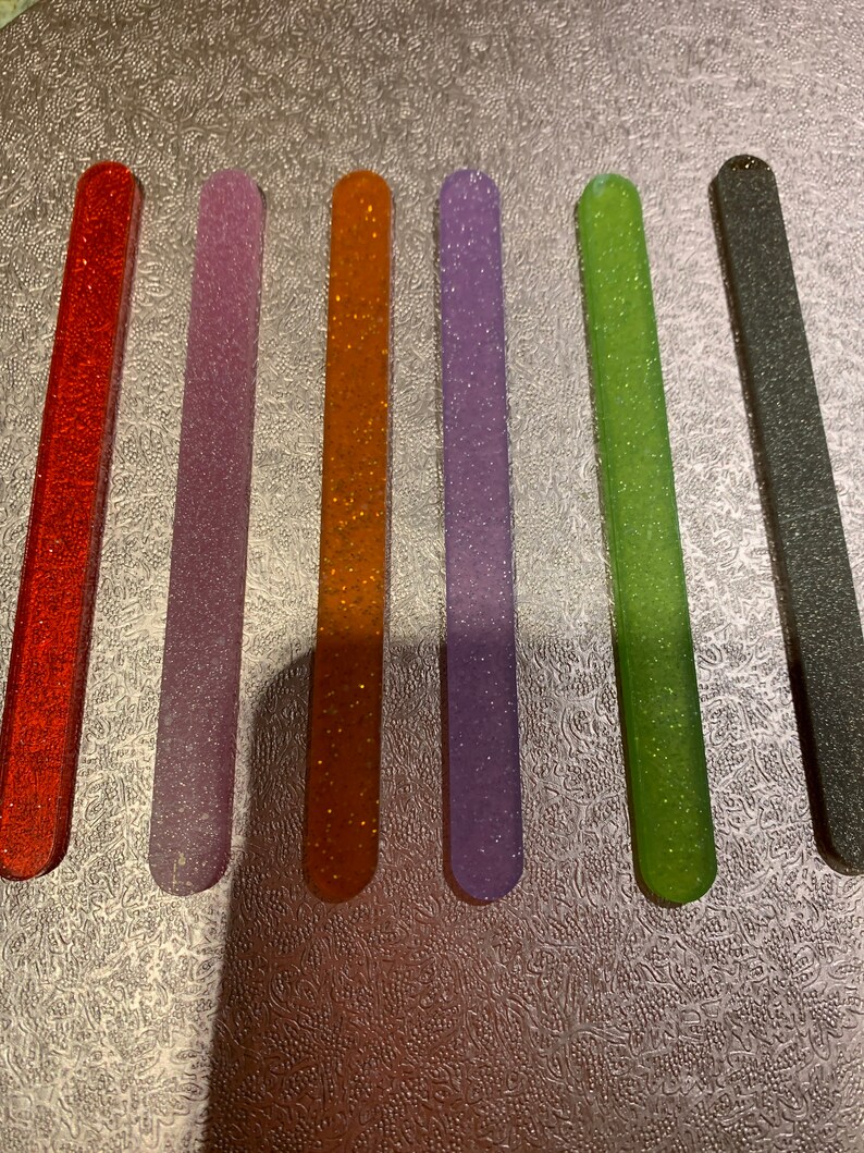 May include: Six nail files with glitter embedded in the surface. The files are in the colours red, purple, orange, lavender, green, and grey.