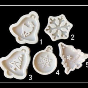 May include: A collection of five white silicone molds in various Christmas shapes. The molds include a bell with a reindeer, a snowflake, a bell with a Christmas tree, a round ornament with a snowflake, and a Christmas tree.