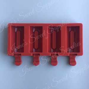 May include: A red silicone ice lolly mould with four rectangular cavities. Each cavity has a central, raised, rectangular channel for the lolly stick. The mould has four small, rounded handles at the base. The background is a light blue.