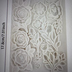 Peut inclure: Moule en silicone floral gris, de 17,8 cm de haut, 12,5 cm de large et 2 cm d'&eacute;paisseur. Le moule pr&eacute;sente une vari&eacute;t&eacute; de fleurs et de feuilles en relief. La couleur est grise.