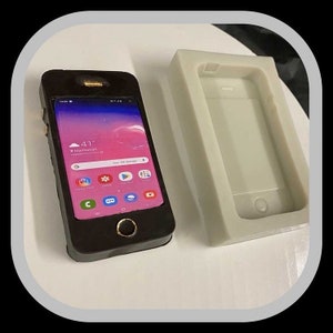 May include: A black phone mockup with a white screen displaying the time and weather in Manhattan. The phone is sitting on a white surface next to a white silicone phone case.
