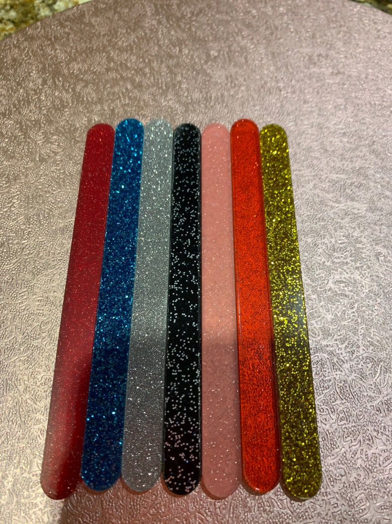 May include: Seven craft sticks covered in glitter, in a variety of colours including red, blue, silver, black, pink, orange and gold.