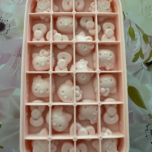 May include: A pink ice cube tray filled with Hello Kitty-shaped molds. The tray is rectangular with multiple compartments, each holding a detailed Hello Kitty design. The overall color scheme is a soft pink, creating a cute and playful aesthetic.
