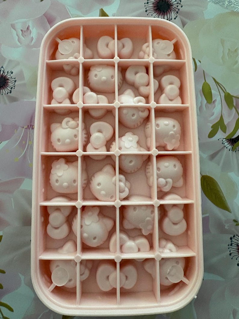 May include: A pink ice cube tray filled with Hello Kitty-shaped molds. The tray is rectangular with multiple compartments, each holding a detailed Hello Kitty design. The overall color scheme is a soft pink, creating a cute and playful aesthetic.