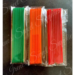 May include: Three packs of wooden craft sticks, each pack containing 10 sticks. The sticks are wrapped in clear plastic and are green, orange, and red.