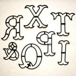 May include: A set of seven black plastic cookie cutters shaped like the letters X, T, R, Q, O, and the ampersand symbol. The cutters are designed with a decorative, ornate style.
