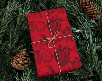 May include: A rectangular gift box wrapped in red paper featuring a repeating black anatomical print of human skulls, hearts, and rib cages. The package is secured with a thin, light-colored twine tied in a simple bow across the center.