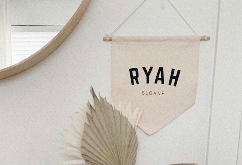 May include: A beige canvas banner with the name "RYAH SLOANE" printed in black block letters.