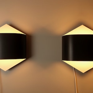 Può includere: Due applique da parete nere e bianche con un design geometrico. Le applique hanno un paralume bianco a forma di diamante e un paralume nero curvo.