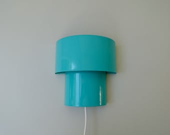 May include: A turquoise blue wall lamp with a cylindrical base and a round shade. The lamp has a white cord.