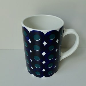 Peut inclure: Une tasse en céramique blanche avec un motif géométrique bleu et vert. Le motif présente des cercles et des diamants.