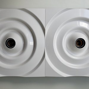 Puede incluir: Dos l&aacute;mparas de pared cuadradas blancas con un dise&ntilde;o circular empotrado y una sola bombilla en cada una.