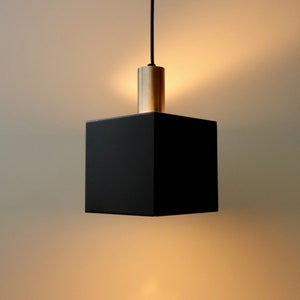 May include: A black square pendant light with a brass finish. The light is hanging from a black cord.