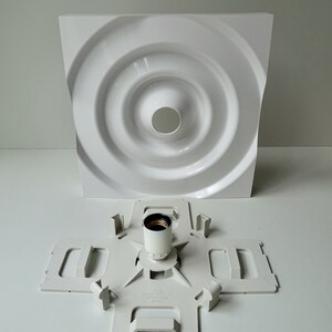 Puede incluir: Luminaria de techo de pl&aacute;stico blanco con un dise&ntilde;o circular y un casquillo de pl&aacute;stico blanco. La luminaria est&aacute; desmontada y el casquillo est&aacute; separado de la parte principal de la luminaria.