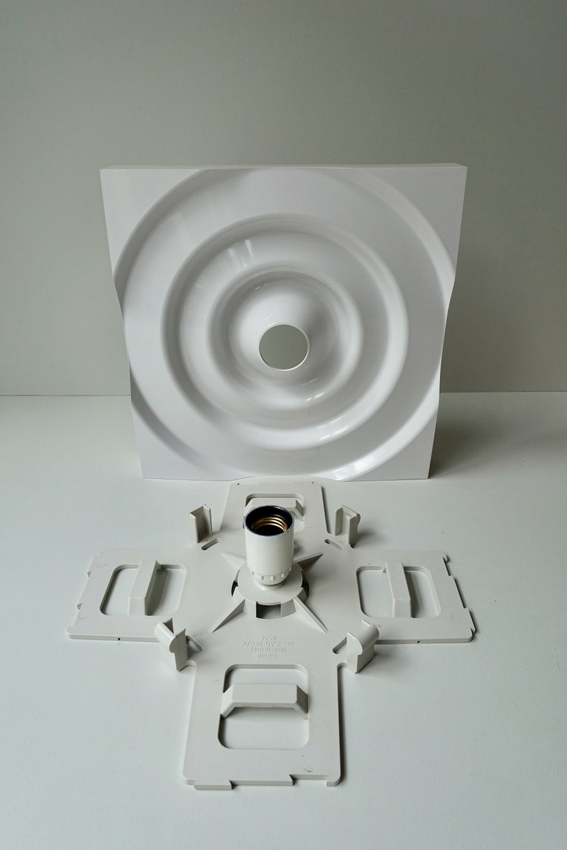 Puede incluir: Luminaria de techo de pl&aacute;stico blanco con un dise&ntilde;o circular y un casquillo de pl&aacute;stico blanco. La luminaria est&aacute; desmontada y el casquillo est&aacute; separado de la parte principal de la luminaria.