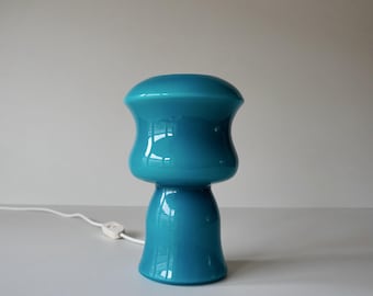 May include: A teal blue glass table lamp with a rounded, bell-shaped shade and a wide base.