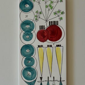 Op de afbeelding: Wit keramisch snijplank met een gestileerd ontwerp van groenten en bloemen. Het ontwerp is in de kleuren groen, blauw, rood en geel.