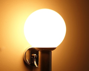 May include: A chrome wall sconce with a white globe-shaped light fixture. The light is on and casting a warm glow.