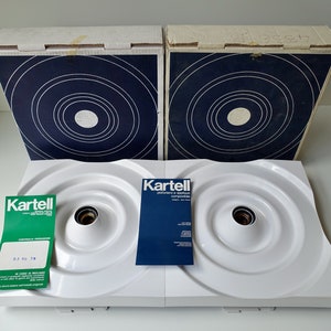 Puede incluir: Dos l&aacute;mparas de techo blancas Kartell con dise&ntilde;os circulares y una caja azul y blanca con el logotipo de Kartell. Las cajas tienen un dise&ntilde;o de c&iacute;rculos conc&eacute;ntricos en azul y blanco.