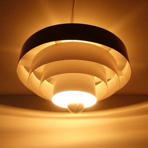 May include: A white ceiling light fixture with a circular design and multiple layers. The light is on and casting a warm glow.