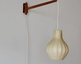 May include: A wall-mounted light fixture with a wooden arm and a white pleated fabric shade. The shade hangs from a white cord.