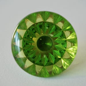 Könnte beinhalten: Ein grüner Glasknopf mit geometrischem Muster. Der Knopf hat eine erhabene Mitte und einen klaren Glasrand.